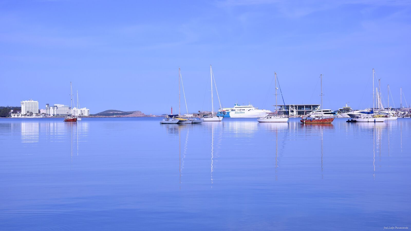 Panoramic view of a calm Sant Antoni bay with small boats moored and a promenade in evening light