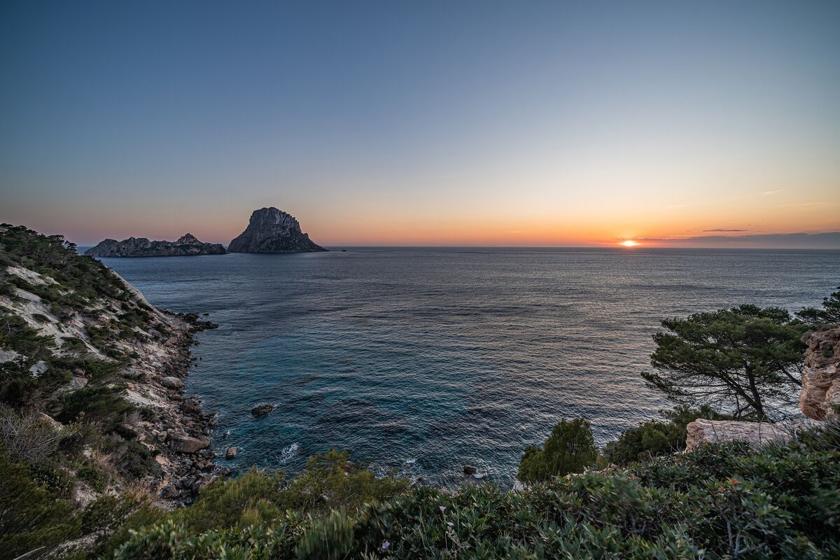 The dramatic Es Vedrà rock island seen from a red-earth cliff with pines at sunset, west coast of Ibiza