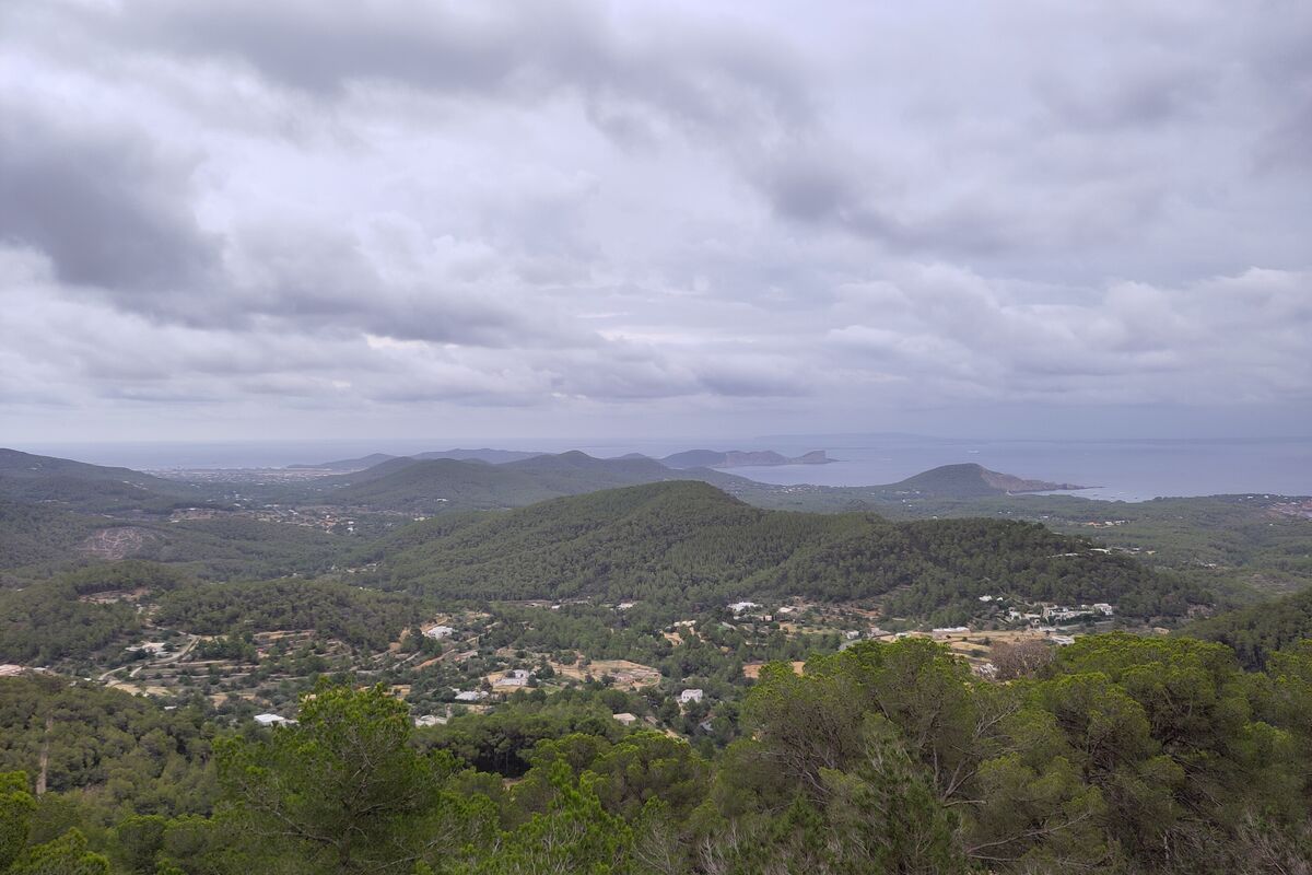 A hiker on a coastal path above the sea on Ibiza with pine trees and cliffs stretching to the horizon